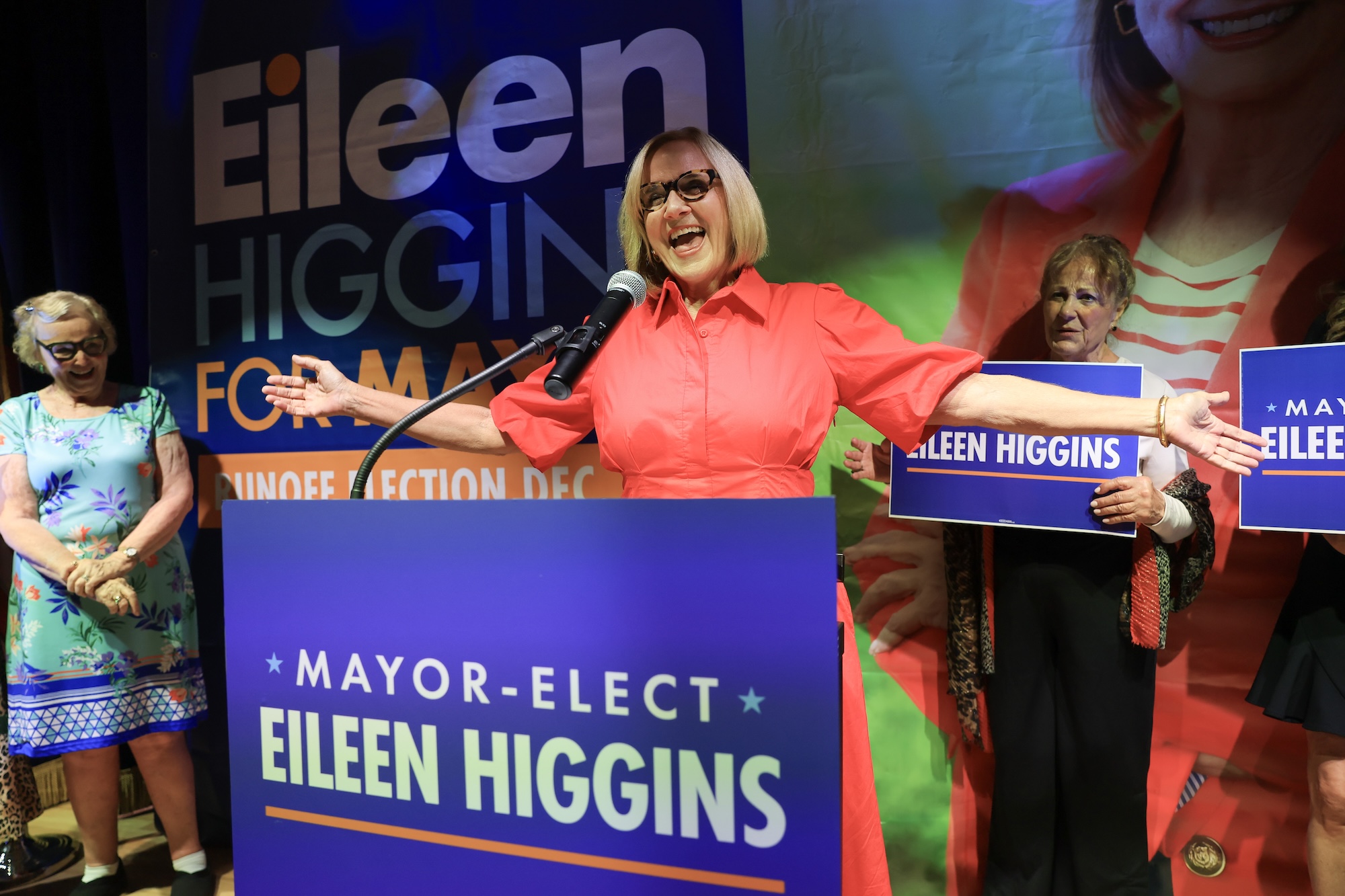 a beaming Eileen Higgins greets supporters from the podium that features a large poster that reads "MAYOR-ELECT EILEEN HIGGINS"