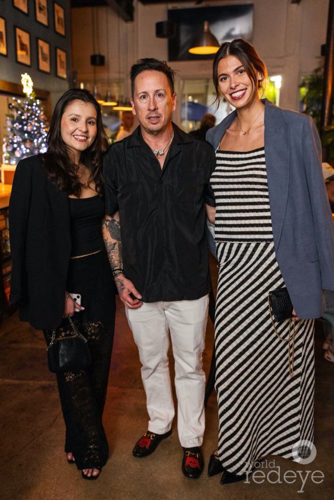 photo of two women posing on either side of a man inside a restaurant
