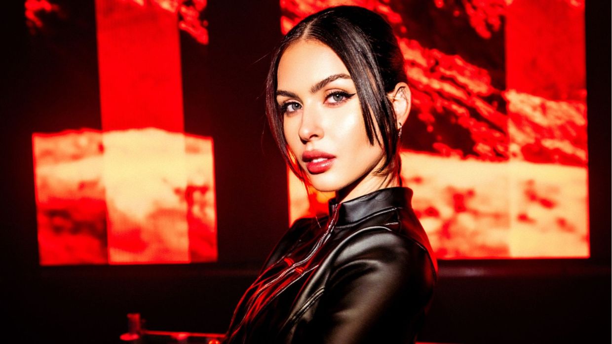 Photo of a woman wearing black against a red LED screen