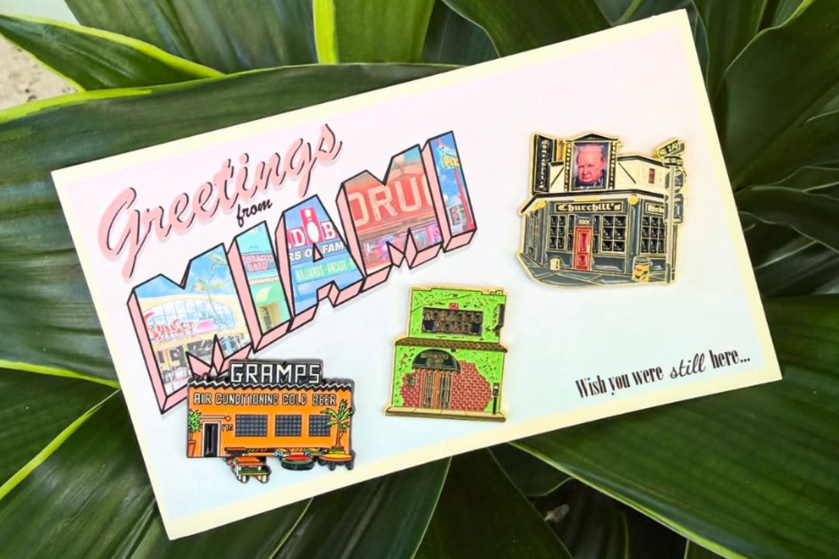 Photo of a postcard that says greetings from Miami and has pins on it.