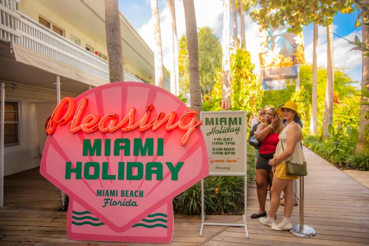 photo of a wooden sign of a sign painted like a pink seashell reading "Pleasing Miami Holiday, Miami Beach Florida"