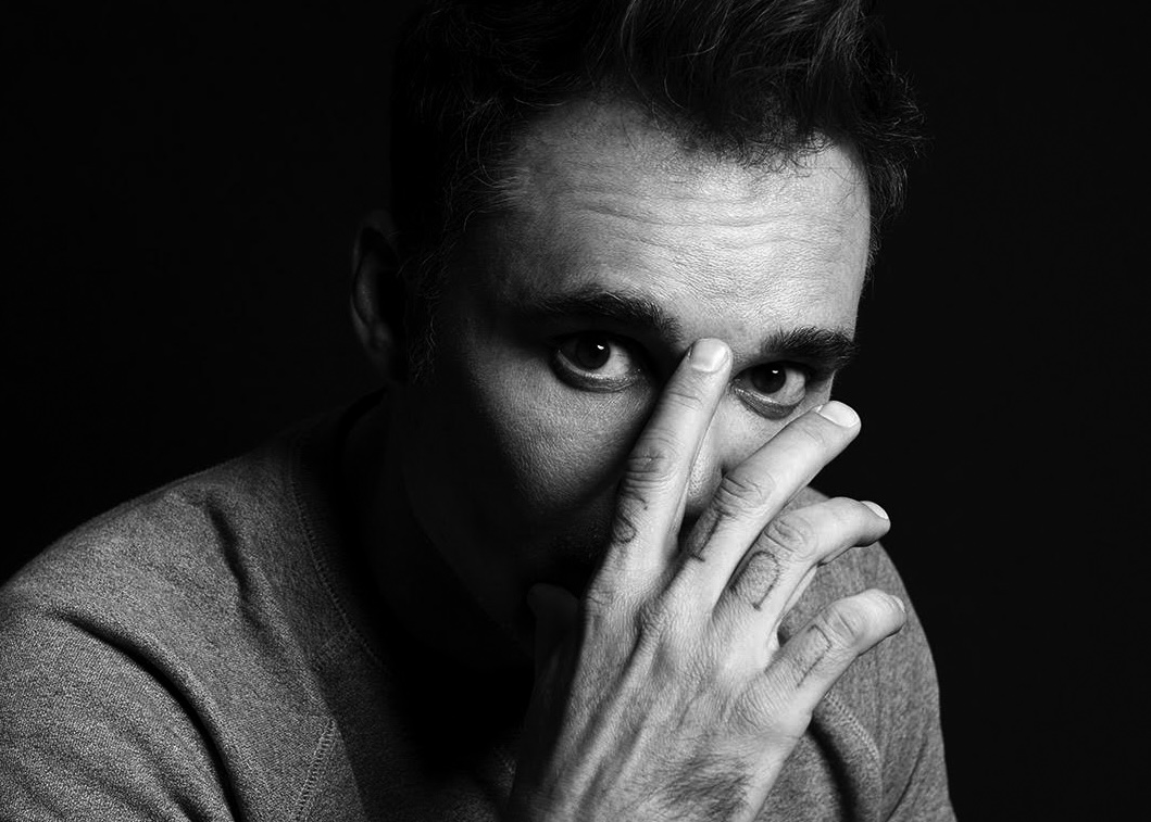 black-and-white portrait of artist David LaChapelle looking through his fingers