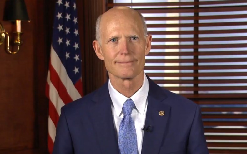 Rick Scott looking at the camera with a soft smile. He is wearing a blue tie and a blue sport jacket.