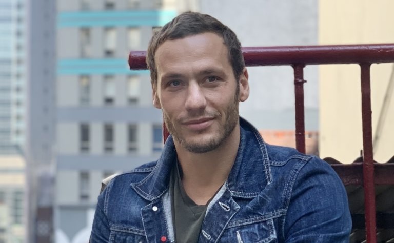 photo of a man in a blue-jean jacket poses with his arms folded