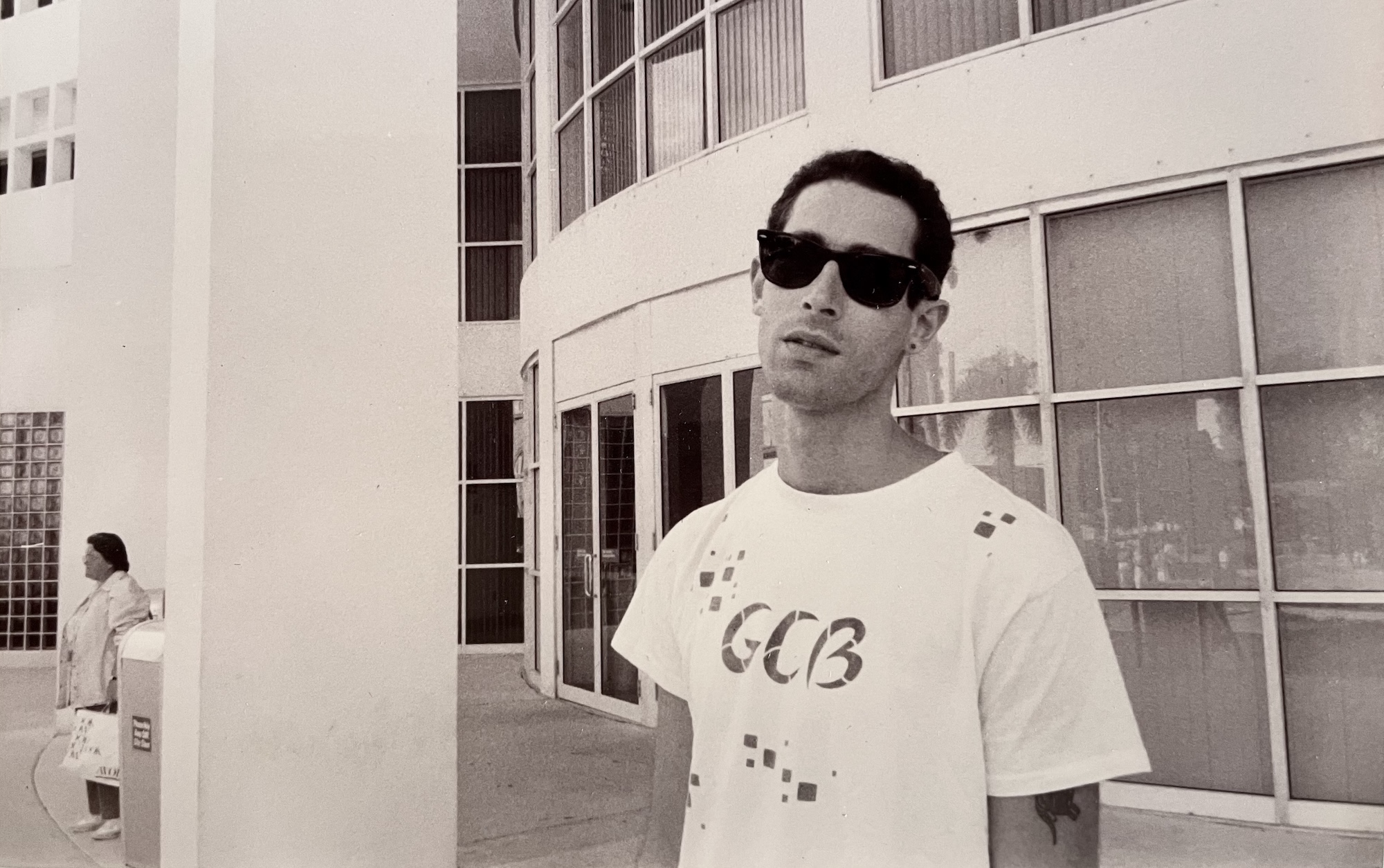 archival black-and-white photo of a young man in a T-shirt and Ray-Ban Wayfarer sunglasses giving the photographer the side-eye