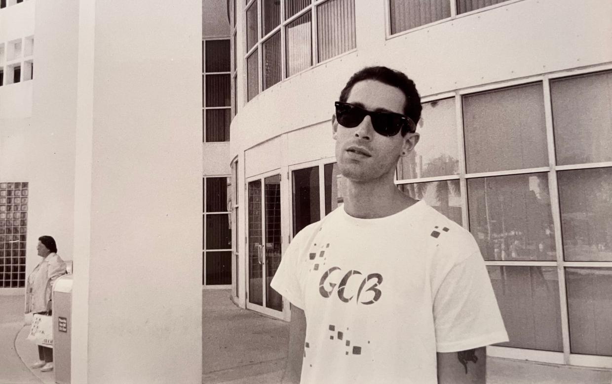 archival black-and-white photo of a young man in a T-shirt and Ray-Ban Wayfarer sunglasses giving the photographer the side-eye