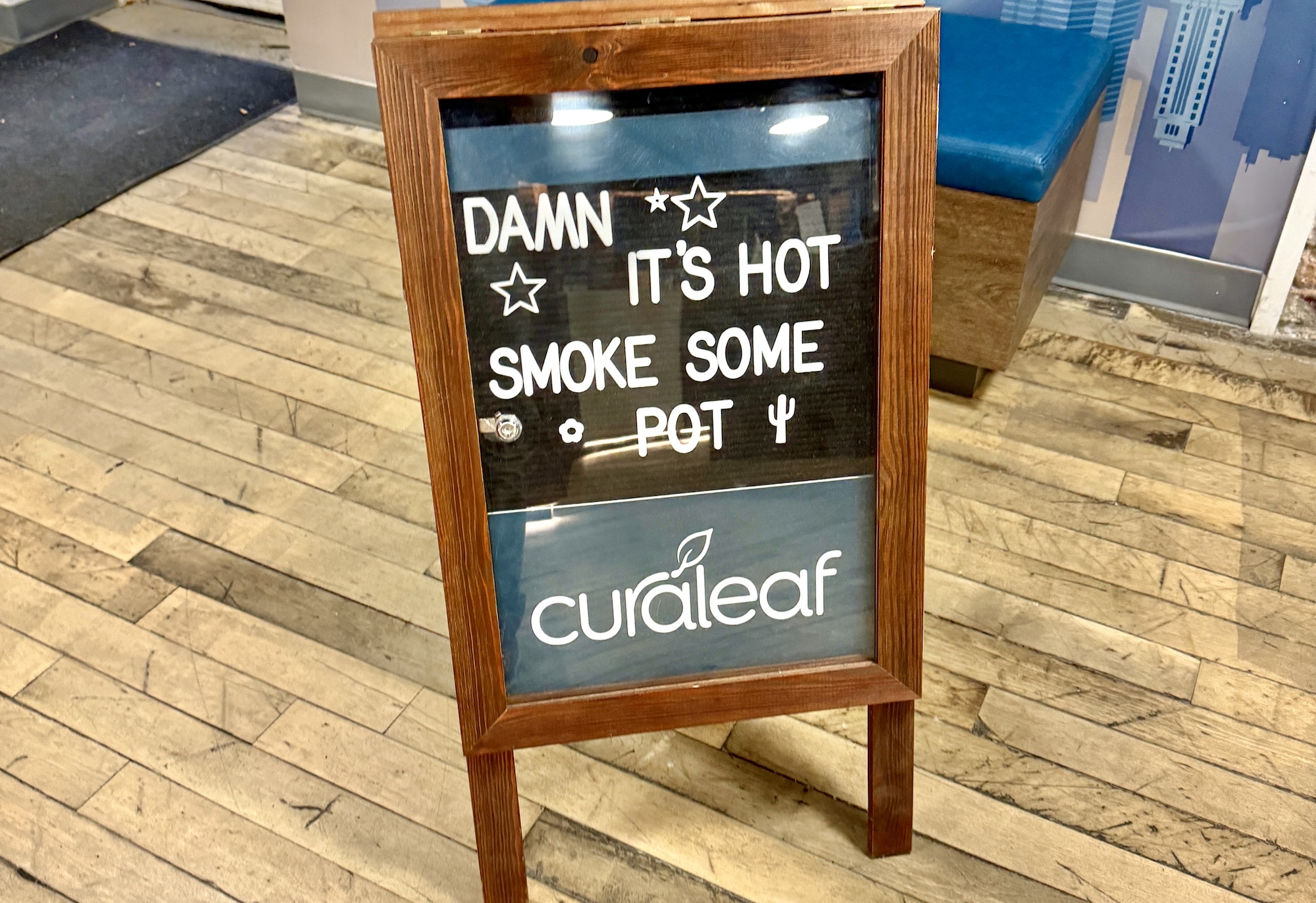 a sandwich board sign that reads "Damn It's Hot, Smoke Some Pot" with the Curaleaf logo underneath