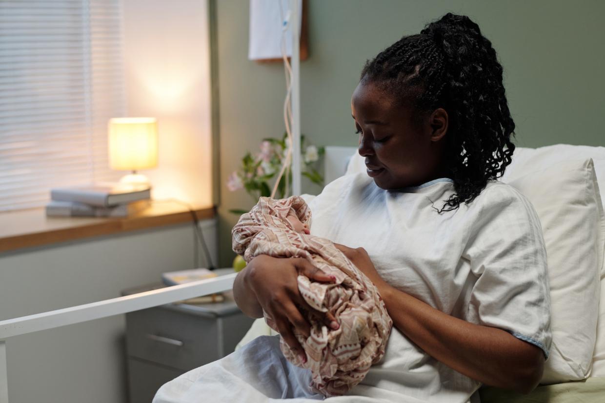 woman cradling swaddled newborn baby in hospital bed