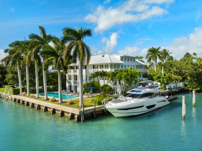 A large white home sits on the ocean, enveloped by palm trees