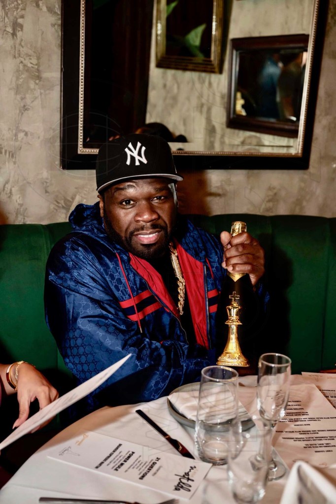 photo of rapper 50 Cent seated at a restaurant table holding a bottle of champagne