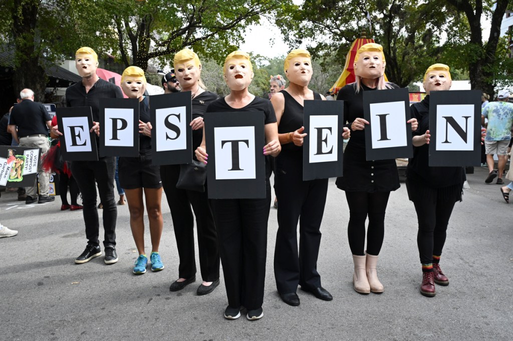 photo of people at a parade wearing Trump masks and holding signs spelling "EPSTEIN"
