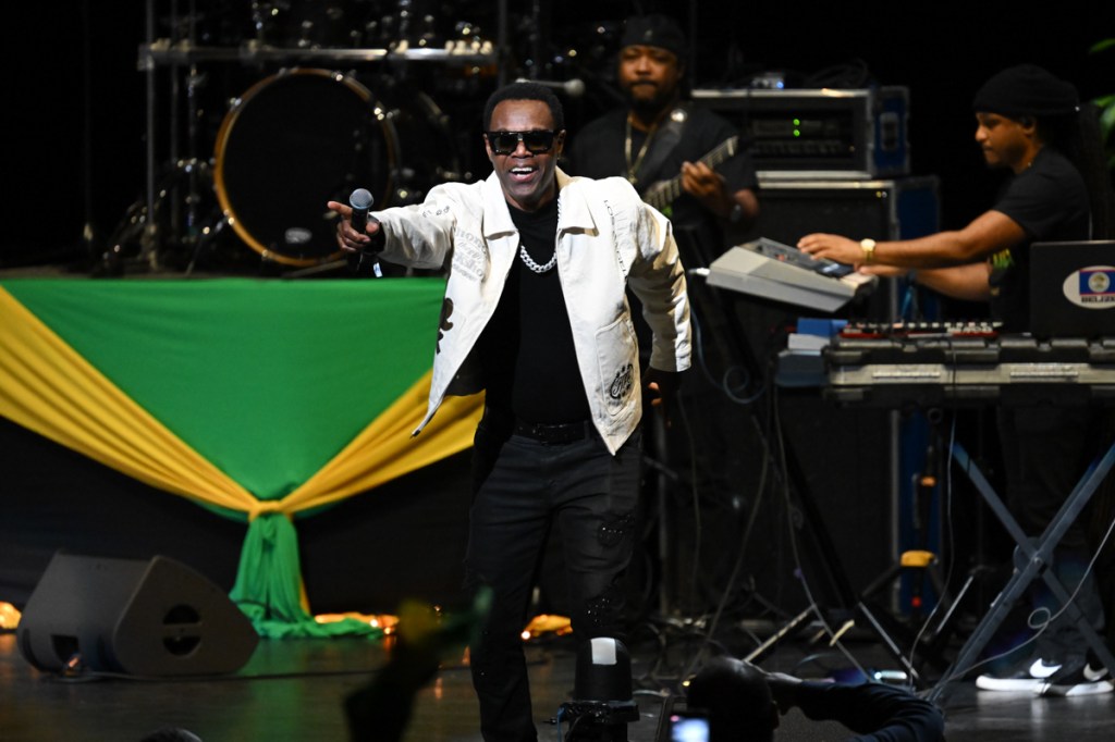A man on stage next to a Jamaican flag 