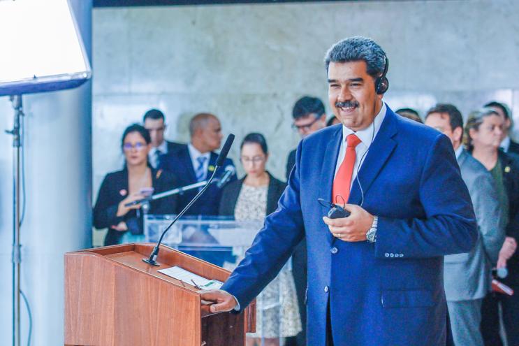 A man with grey hair stands before a podium in a blue suit.