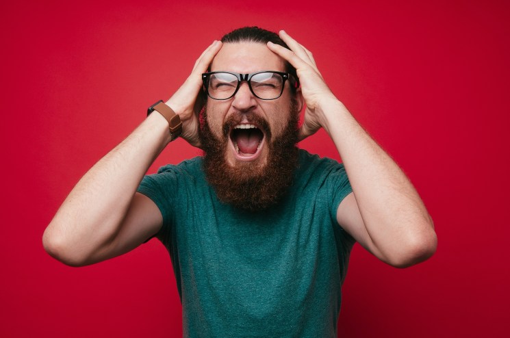 photo of a screaming bearded man looking at the camera with hands on his head