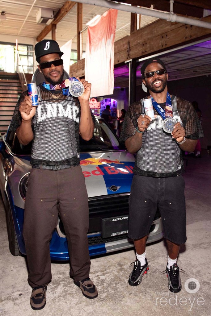 photo of two men posing with Red Bull cans in front of a car with Red Bull branding