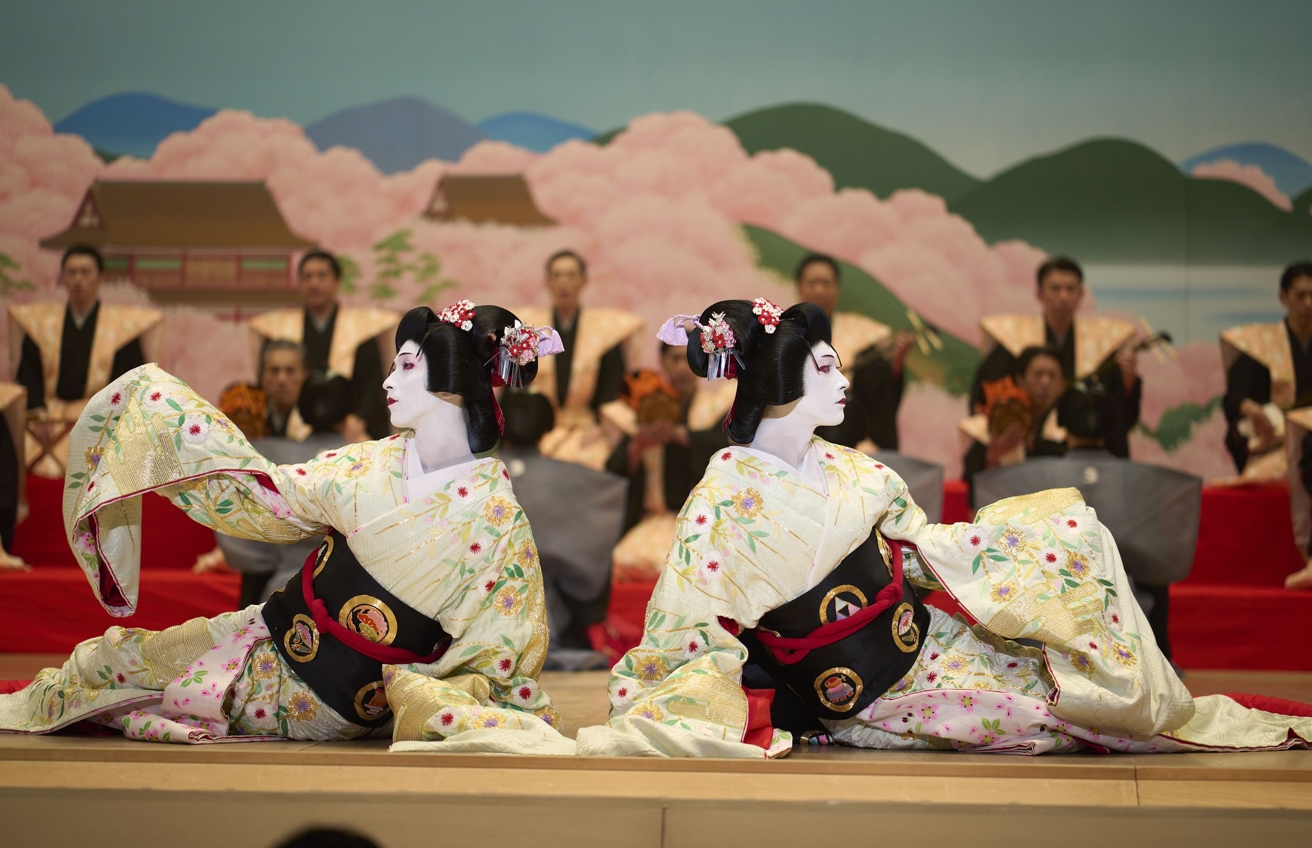 film still showing two geishas on a stage in front of men in uniforms