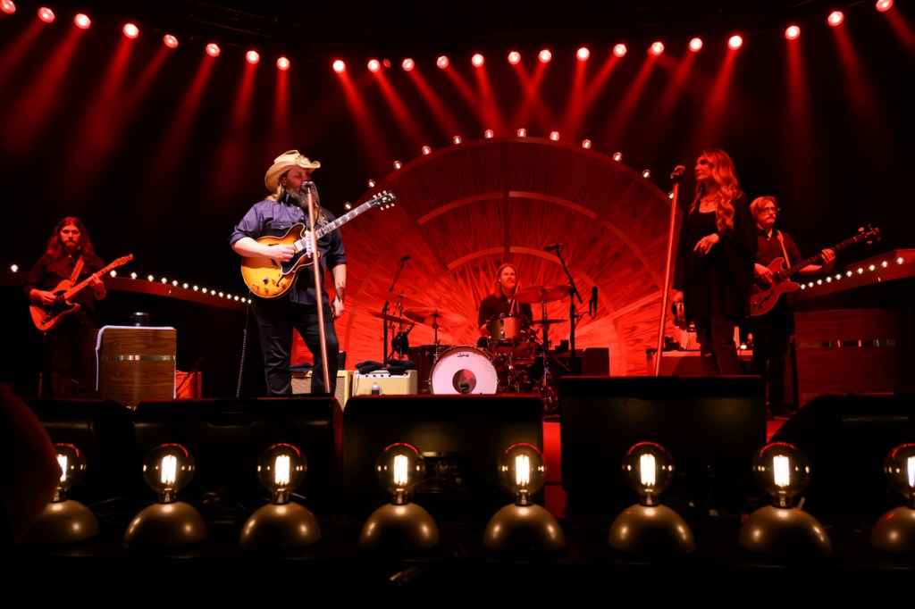 An Americana band performing on stage under red lights. 