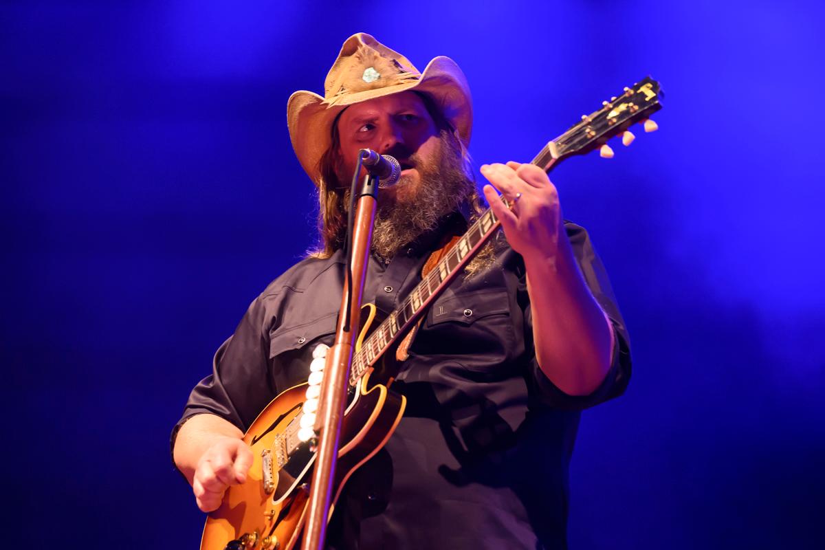 A country singer on stage wearing a cowboy hat and playing the guitar.