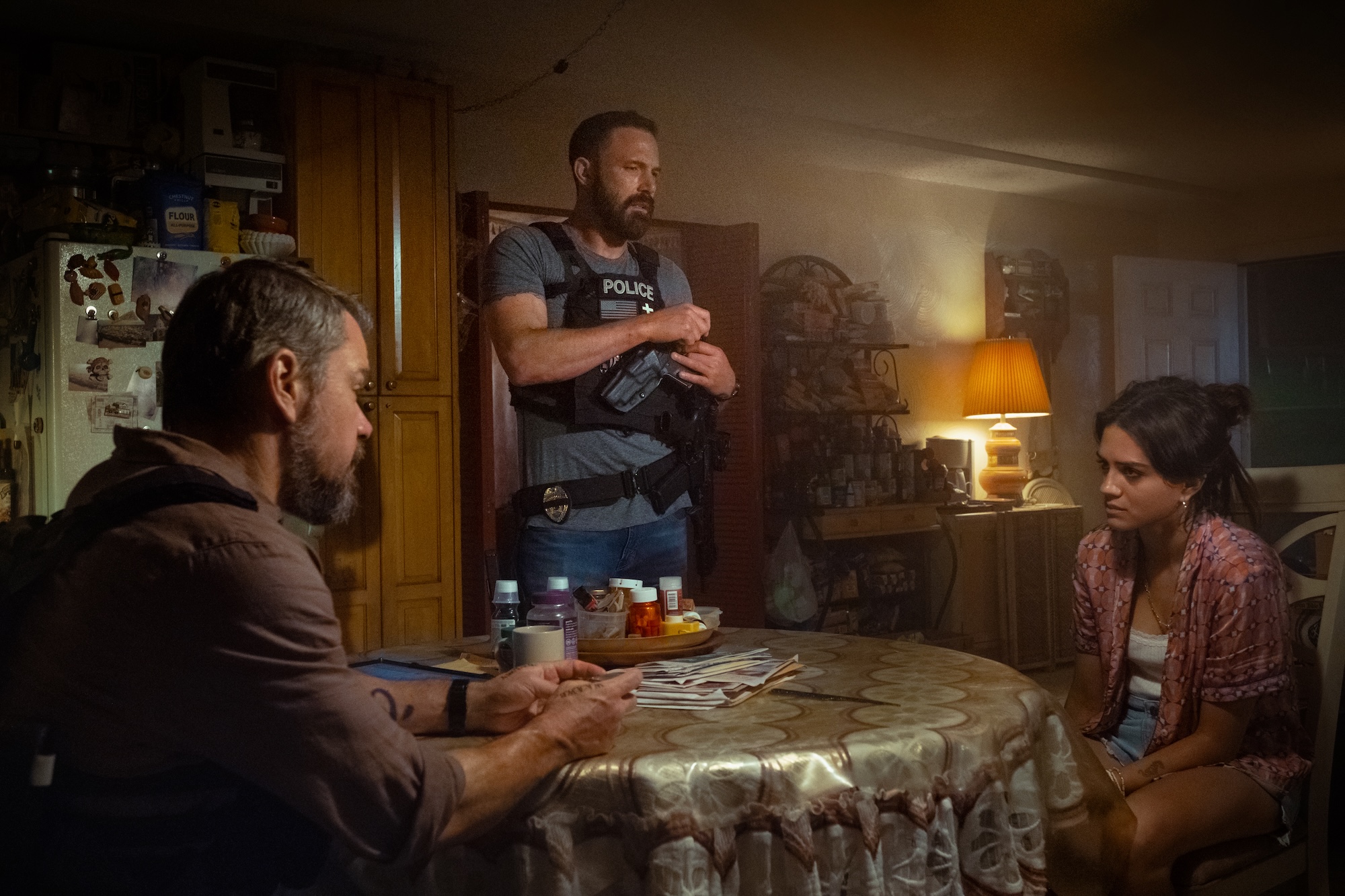 film still of two people at a dining room table speaking to a police officer