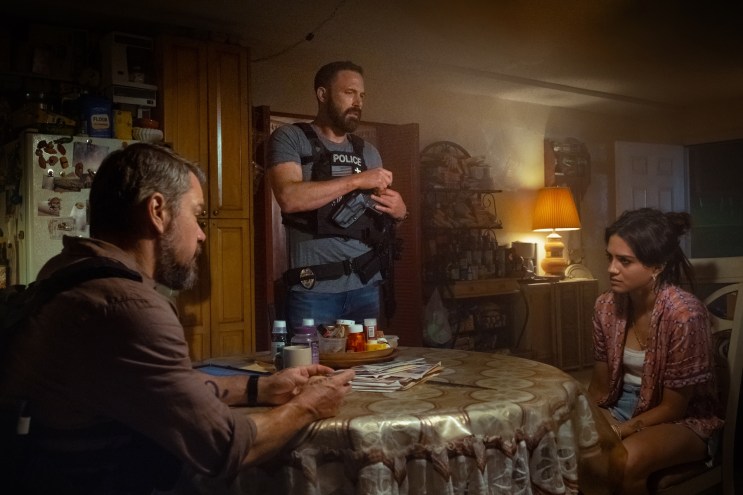 film still of two people at a dining room table speaking to a police officer