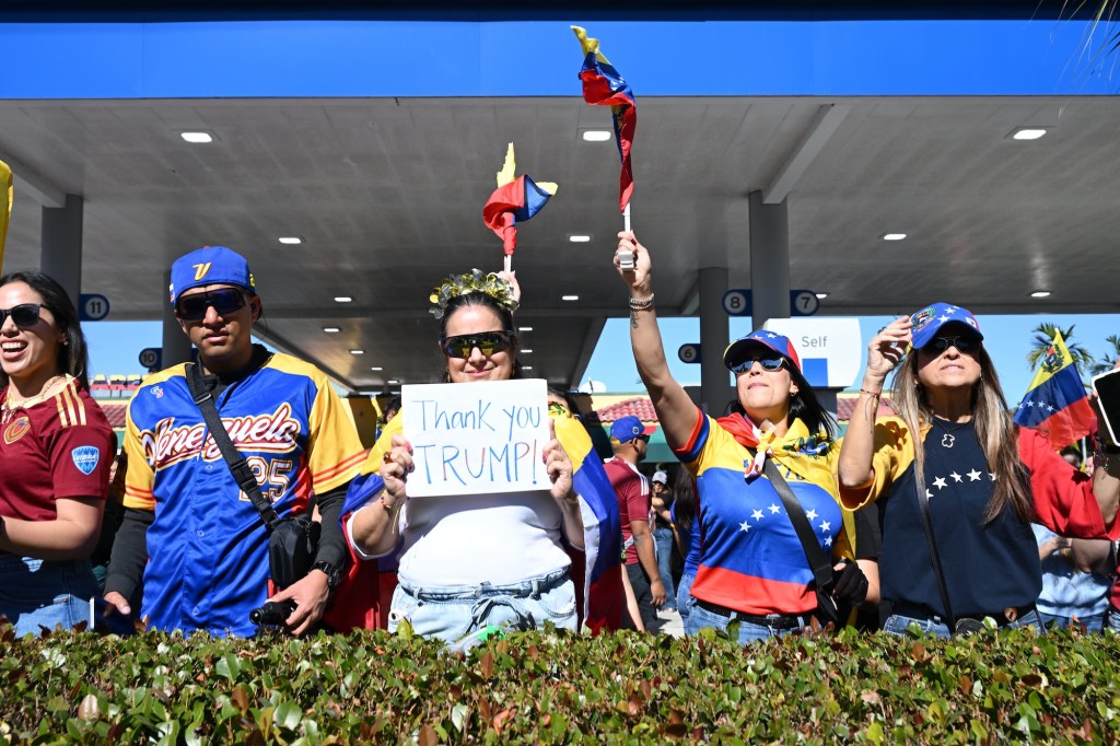 photo of protesters wearing clothes with the Venezuelan flag and waving Venezuelan flags. A woman in the center holds a sign reading, "Thank you Trump"