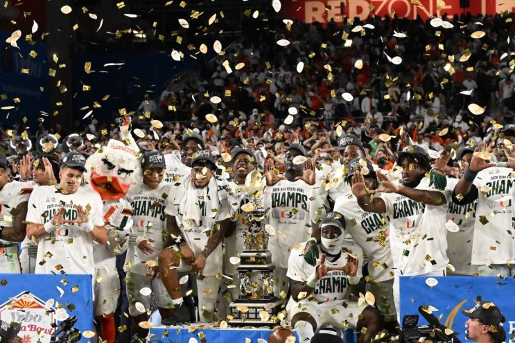 Miami Hurricanes players flash "the U" on the stage at the Fiesta Bowl alongside Sebastian the Ibis mascot. There is confetti coming down as well.