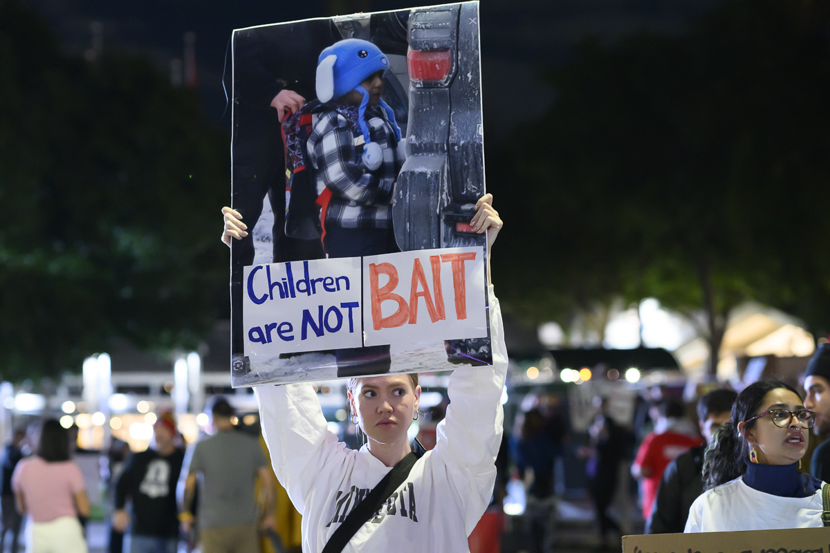 photo of a protester holding sign with a photo of a toddler and text reading, "children are not bait"