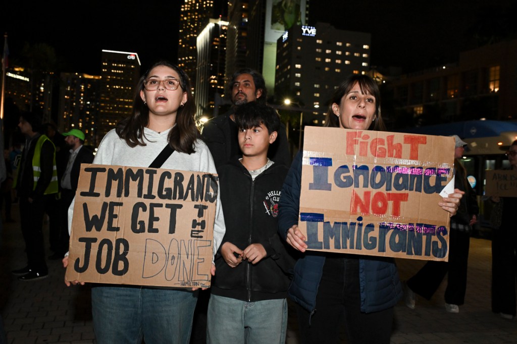 Photo of a crowd of protesters. The protesters in the crowd hold signs reading, "Immigrants, we get the job done" and "fight ignorance, not immigrants"