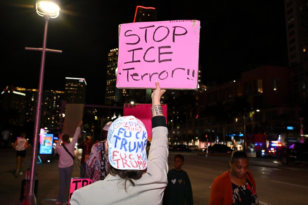 photo of a man wearing a backwards baseball cap reading, "fuck Trump" in marker holding a sign reading, "Stop ICE terror"