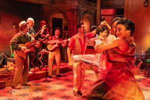photo of a theater production with folkloric musicians in the background and two couples dancing and twirling in the foreground