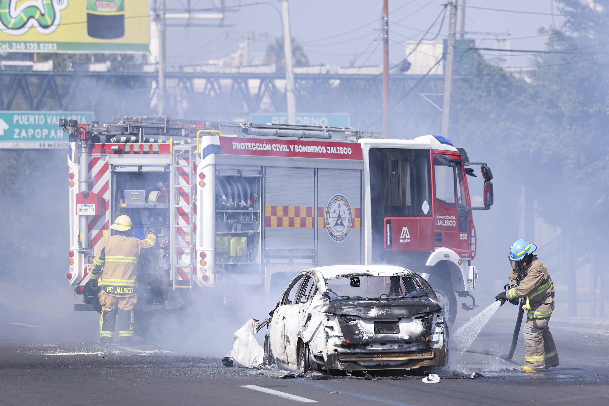 Firefighters in Mexico extinguish a fire surrounding a white car. Smoke fills the air.