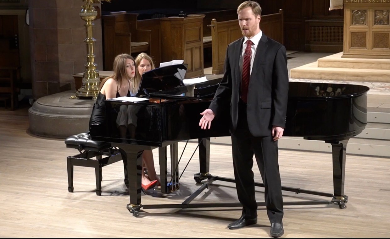 Photo of two women on stage playing piano and a opera singer