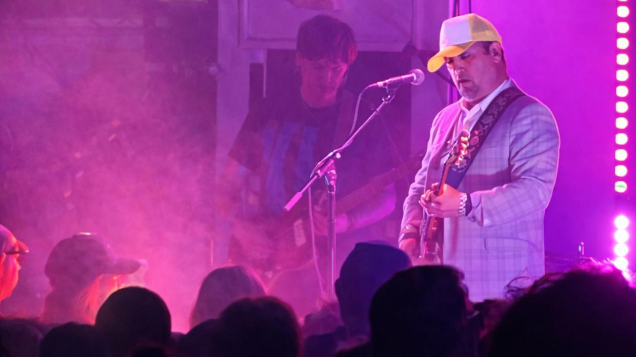 Photo of a band performing on stage under purple lights.
