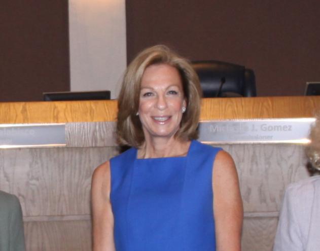 An older woman with short blonde hair and a blue dress smiles for the camera.