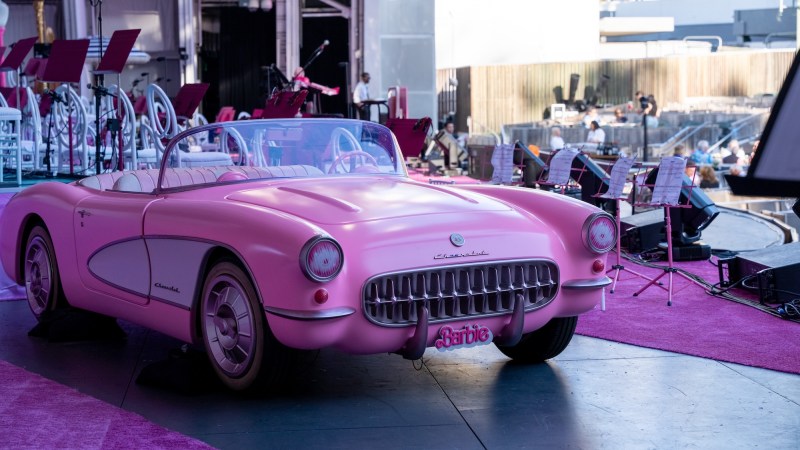 photo of a model pink convertible with a "Barbie" plate on an outdoor stage next to pink carpet and pink music stands