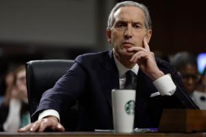 photo of Starbucks CEO testifying in front of a senate committee on Capitol Hill. An out-of-focus Starbucks thermos is in front of him on the desk.