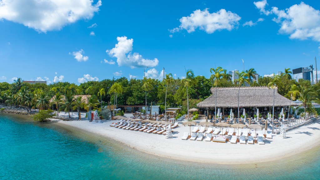 an island surrounded by blue water and a tiki hut on the sand