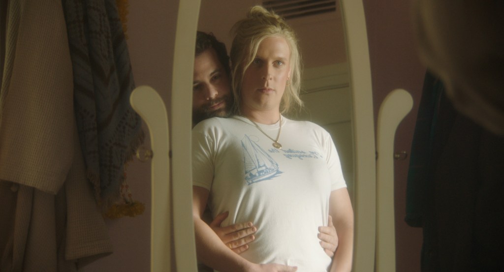 film still from the movie 'Maddie’s Secret' of a man standing behind a woman as they both look in a mirror