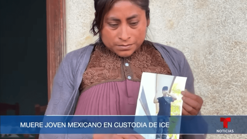 A screenshot of a Telemundo broadcast showing a woman solemnly holding a printed out photo of a child wearing a black Tshirt and pants.