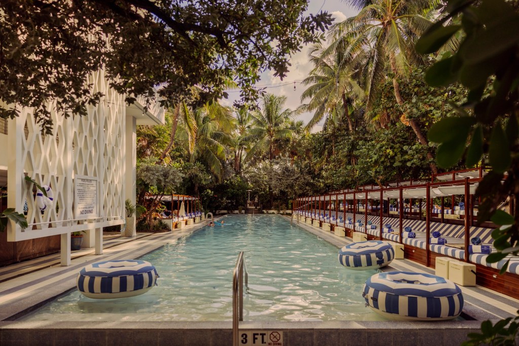 photo of a pool with cabanas and a bar on either site with blue and white pool floaties on the water