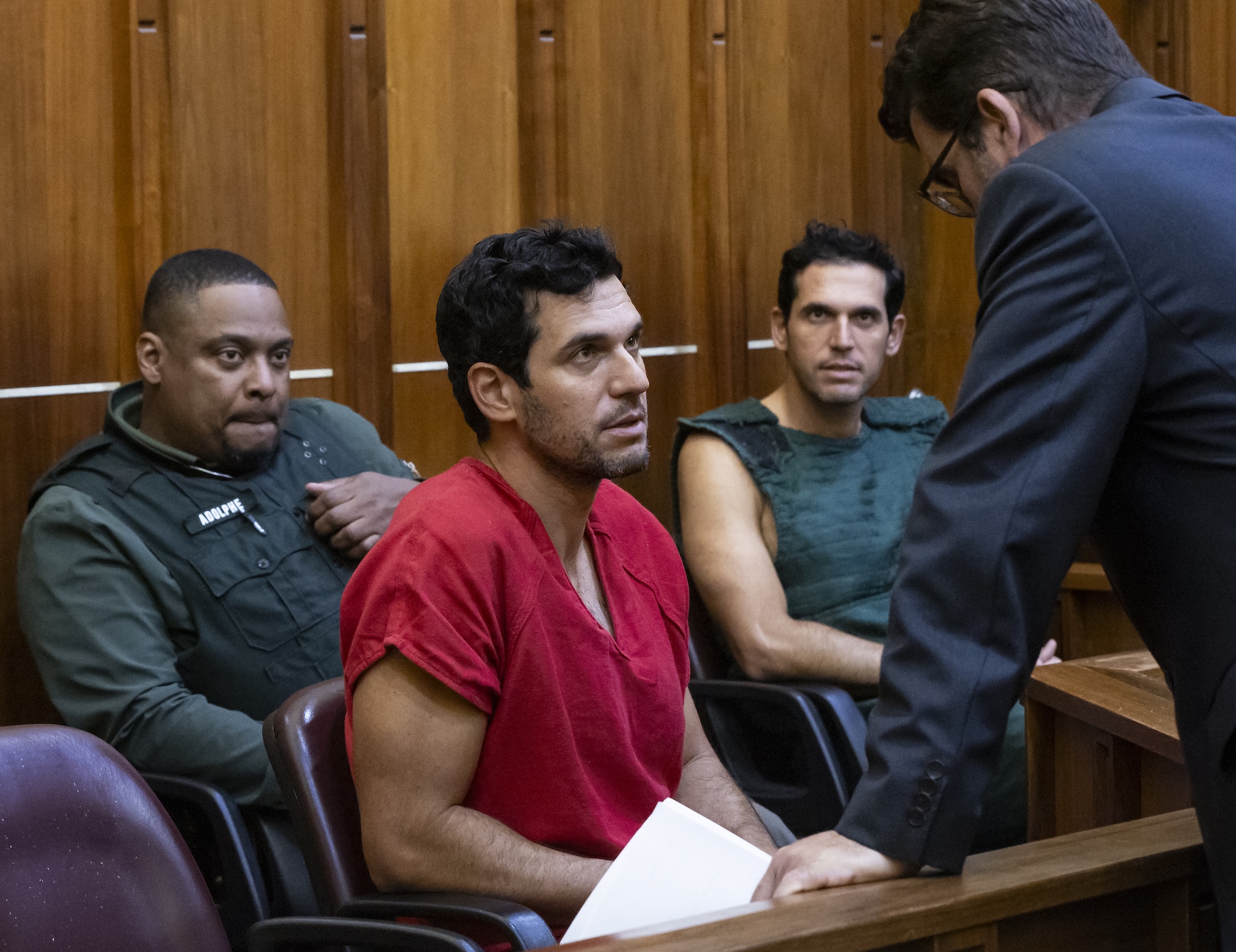 a deputy sits in a courtroom behind two men in shackles