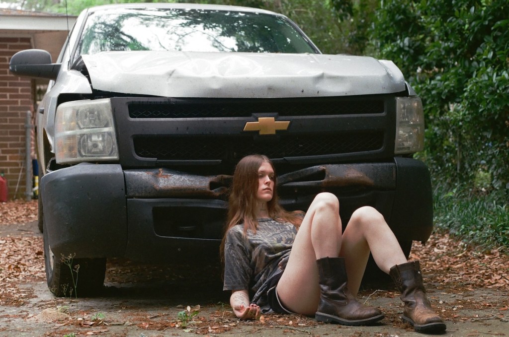 Photo of a person sitting next to a crashed car .
