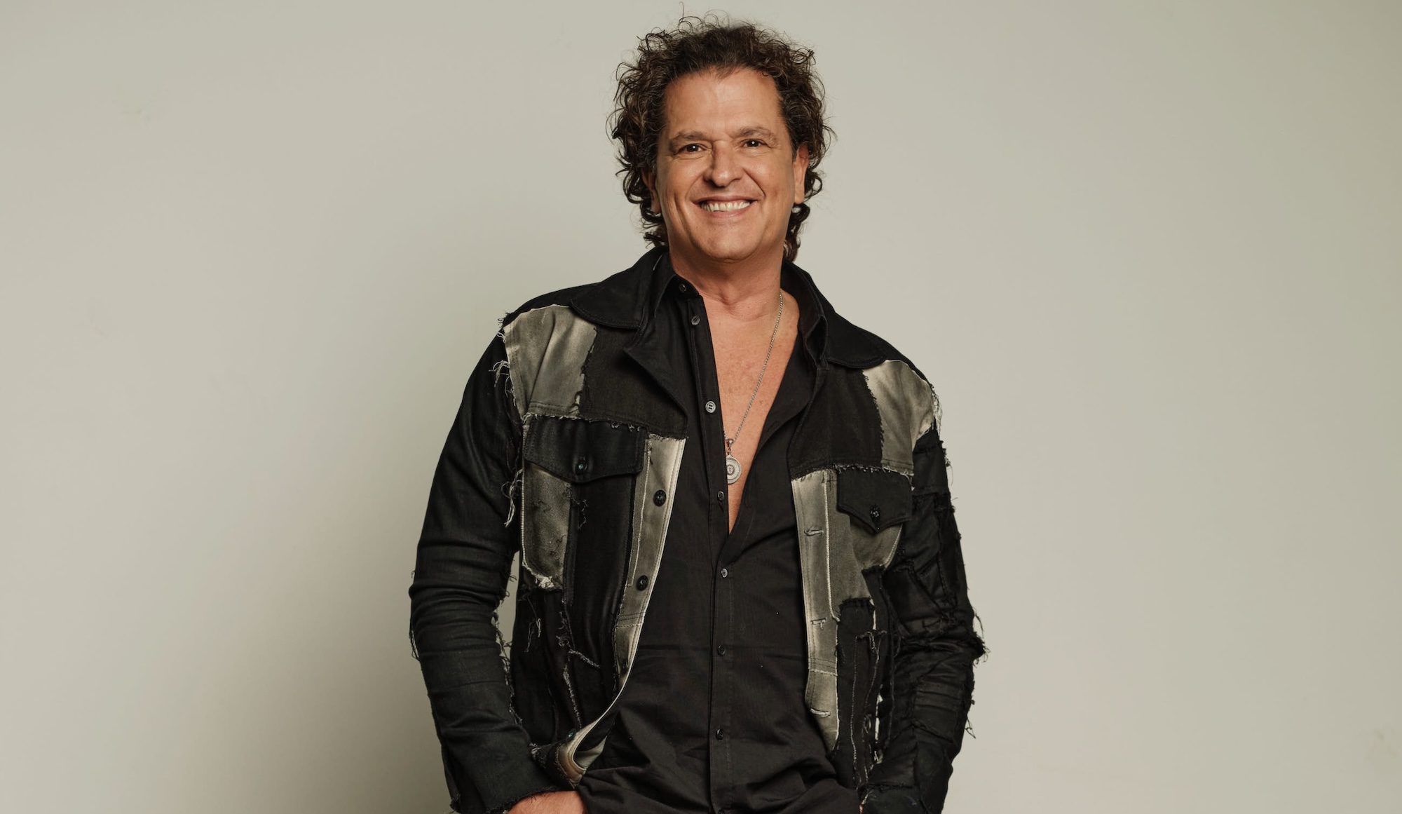 photo of singer Carlos Vives posing in a stylishly tattered blazer posing against a cream-colored backdrop