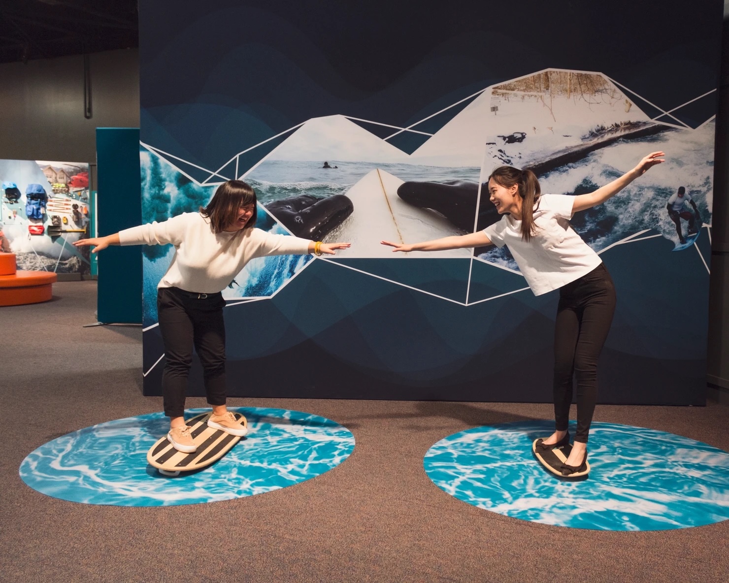 photo of two young girls riding stationary surfboards inside a museum exhibition