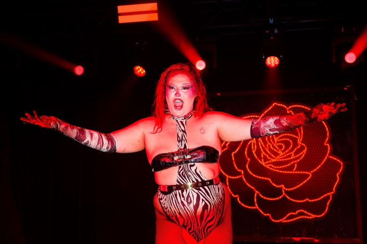 Photo of a performer on stage in front of a rose shaped neon sign.