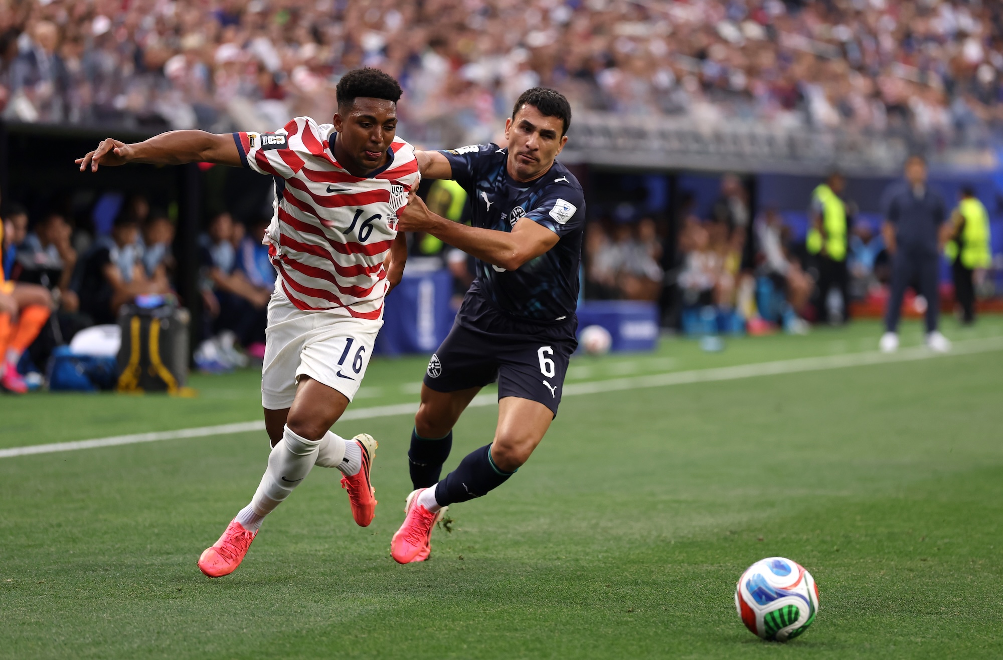 a U.S. soccer player dribbles a ball past a Paraguayan defender on a soccer field