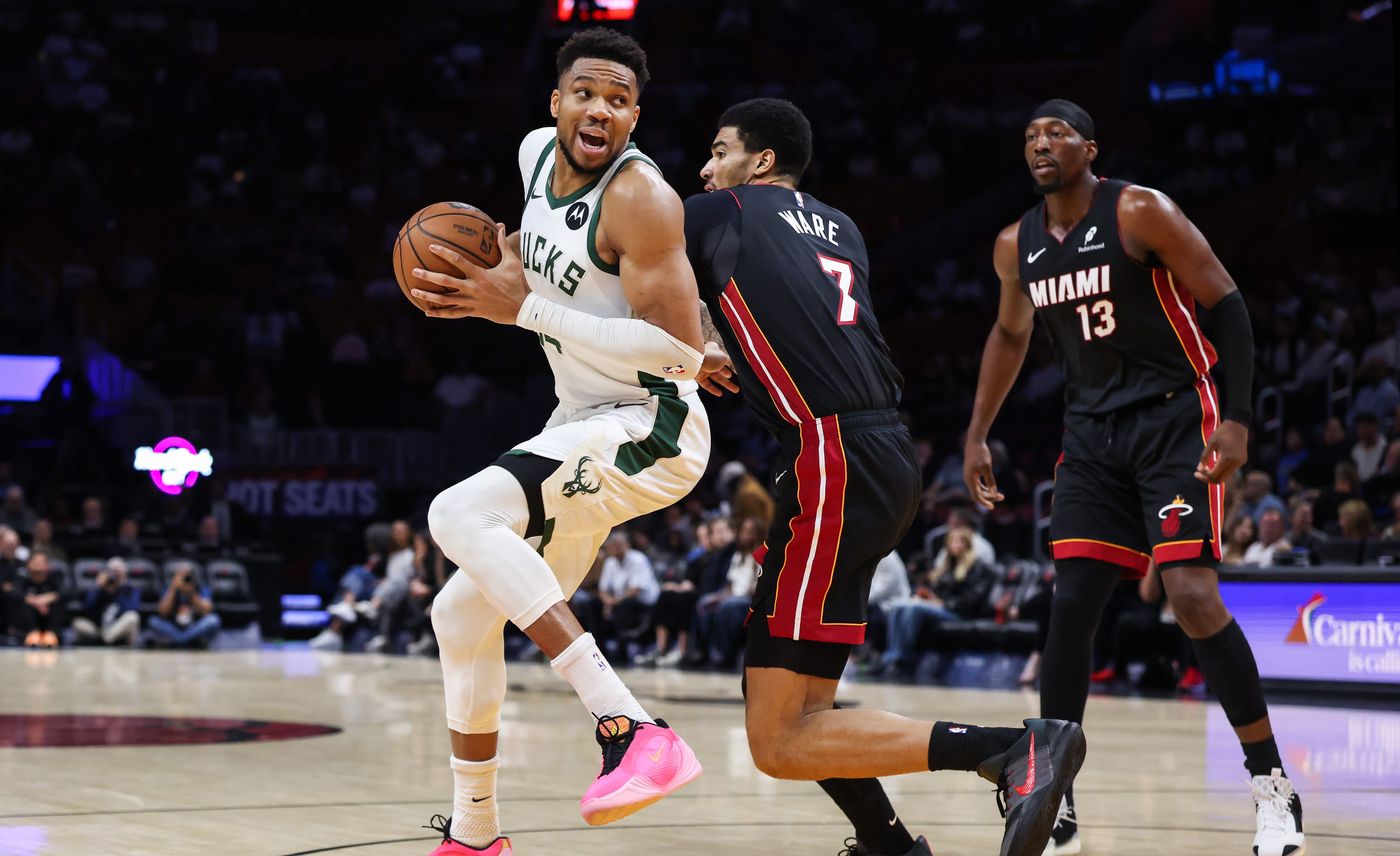 Giannis Antetokounmpo holds the basketball as he plays against two Miami Heat players on the basketball court