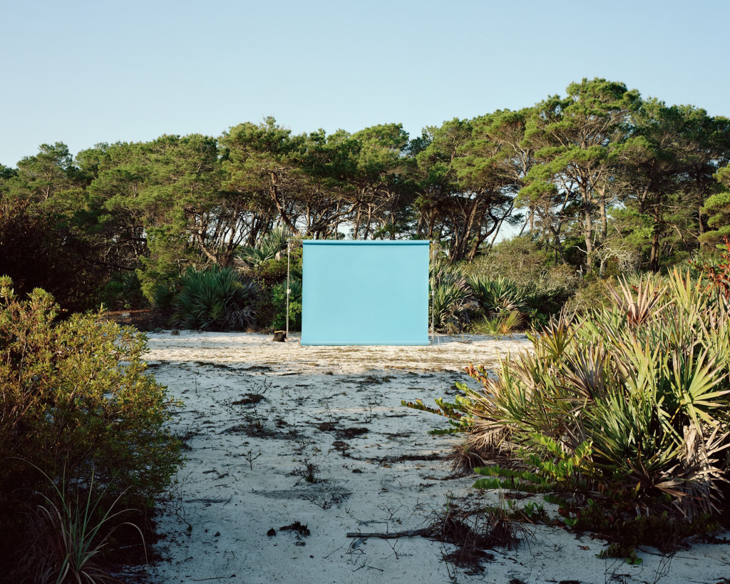 photo of a teal-blue photoshoot backdrop set up on the sand surrounded by trees