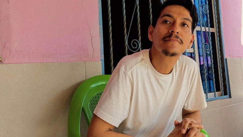 photo of an artist sitting on a green plastic chair in front of a window and pink-and-beige wall