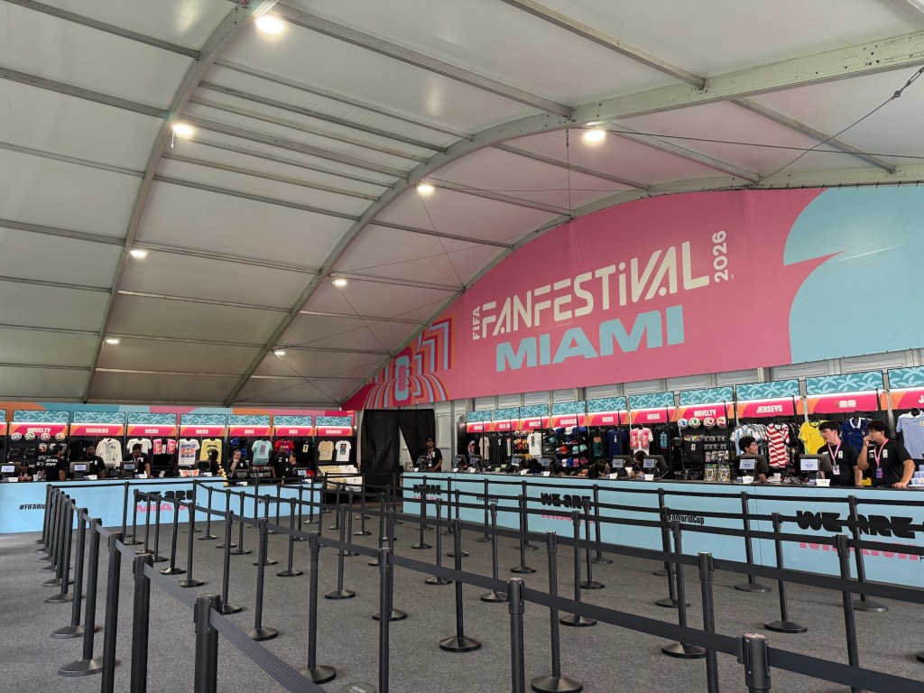 Photo of a merch shop inside a tent. A sign in the background reads "FAN FESTIVAL MIAMI"